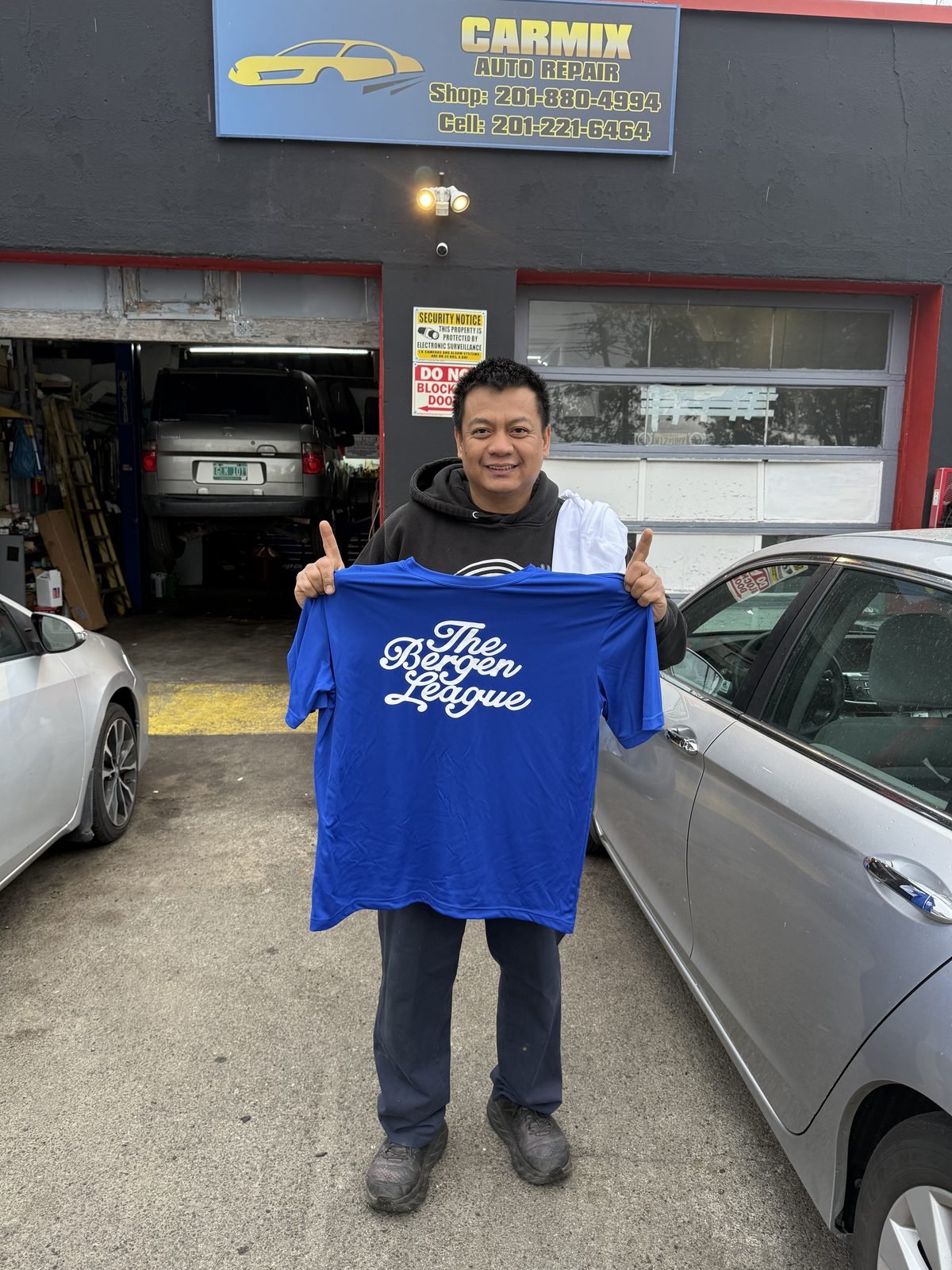 Carmix Auto Repair owner holding a Bergen League shirt outside the garage